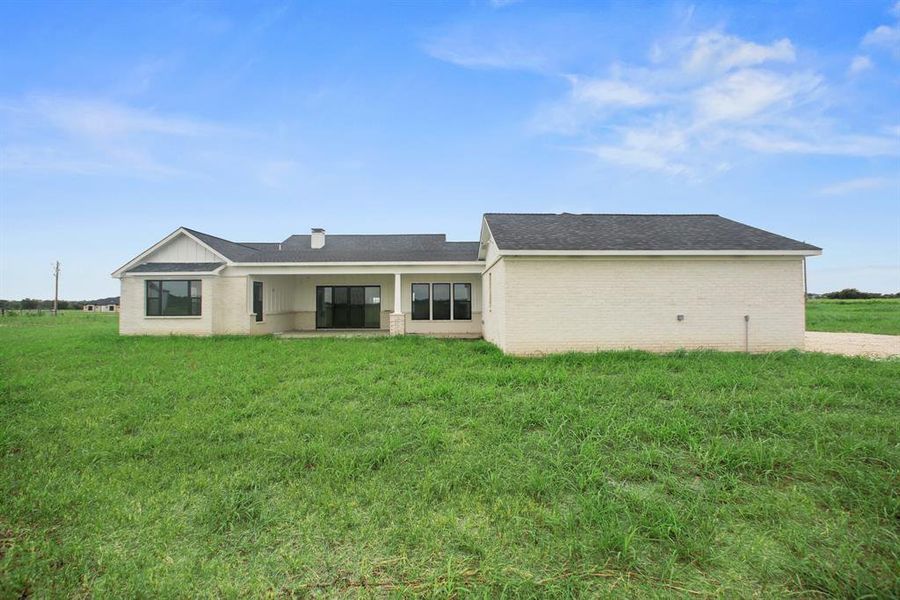 Rear view of property with a shingled roof, a lawn, and brick siding