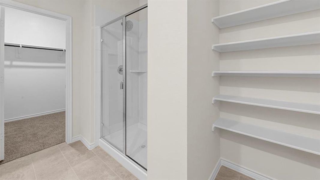Full bathroom featuring a walk in closet, a shower stall, light carpet, and light tile patterned floors