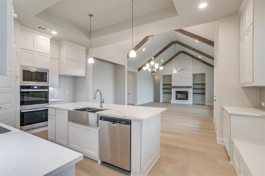 Kitchen with white cabinetry, a fireplace, brick wall, light hardwood / wood-style floors, and appliances with stainless steel finishes