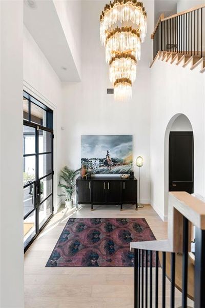 Entryway featuring a towering ceiling, arched walkways, a chandelier, and light wood-style flooring Entryway featuring a towering ceiling, arched walkways, a chandelier, and light wood-style flooring