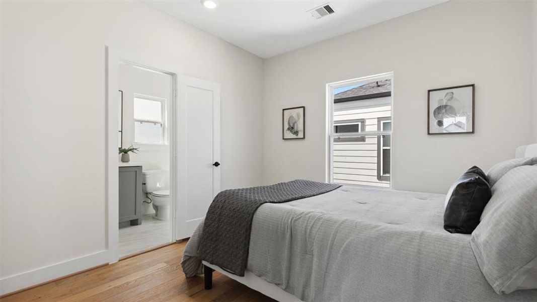 Bright and modern secondary bedroom features engineered hardwood floors, neutral custom color walls, and private secondary en-suite bathroom completed with window providing natural light.