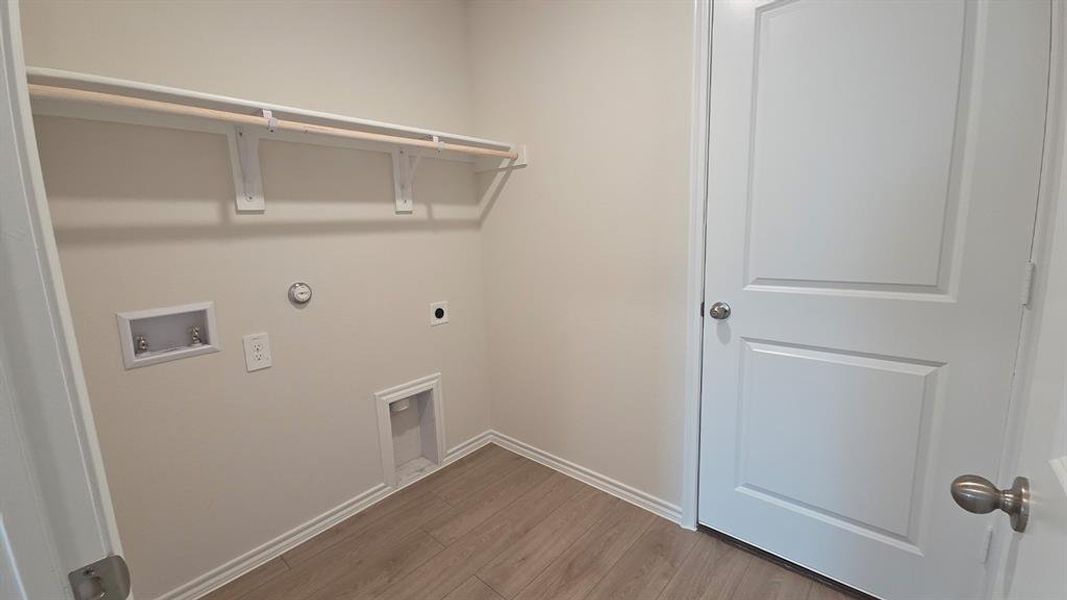 Dedicated utility space with wood-finish flooring, light neutral wall paint, and a built-in hanging rod with shelving Dedicated utility space with wood-finish flooring, light neutral wall paint, and a built-in hanging rod with shelving