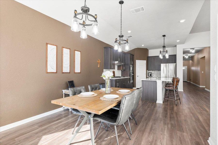 Dining area featuring visible vents, an inviting chandelier, vaulted ceiling, wood finished floors, and baseboards