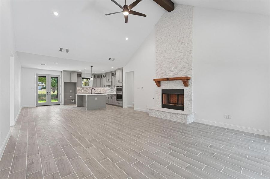 Unfurnished living room with high vaulted ceiling, wood tiled floors, french doors, a fireplace, and a ceiling fan Unfurnished living room with high vaulted ceiling, wood tiled floors, french doors, a fireplace, and a ceiling fan