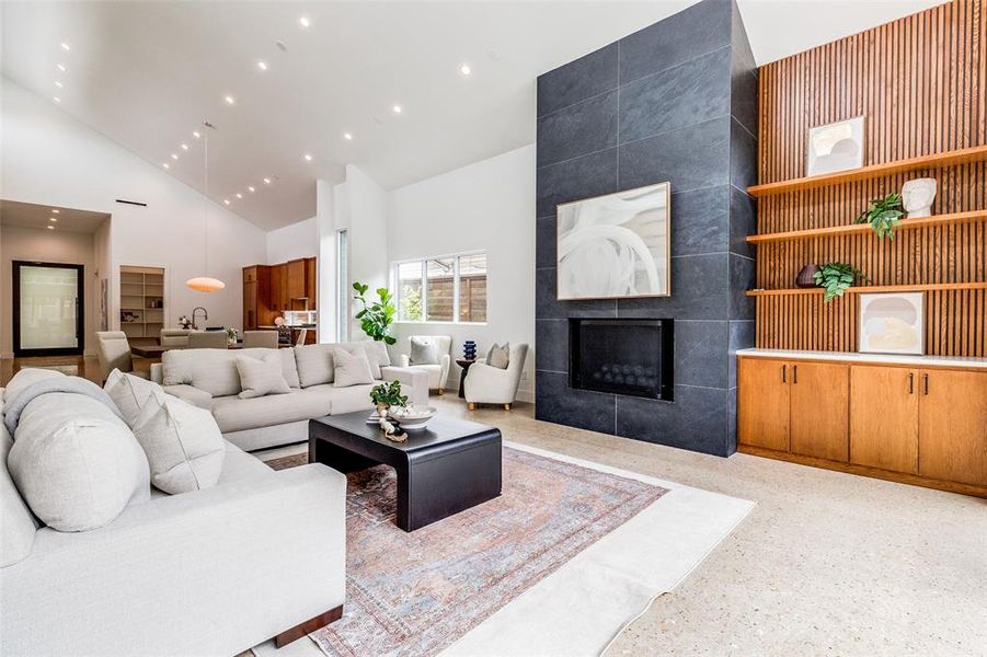 Open concept living room featuring a tile fireplace, chef's kitchen, and high vaulted ceiling