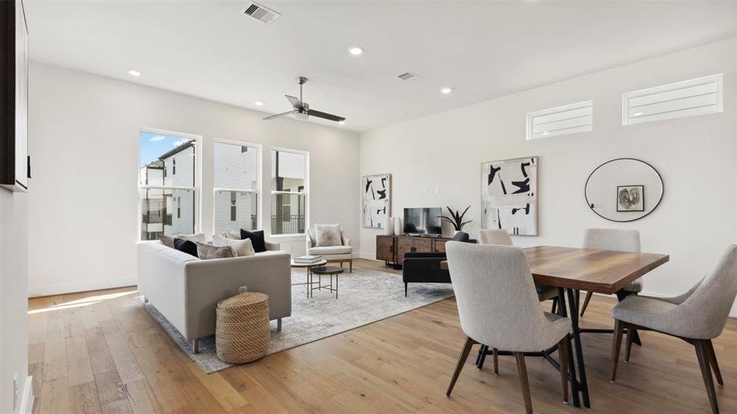 This photo showcases a bright, modern open-concept living and dining area with large windows, wood flooring, and stylish furnishings, creating a welcoming and spacious environment.