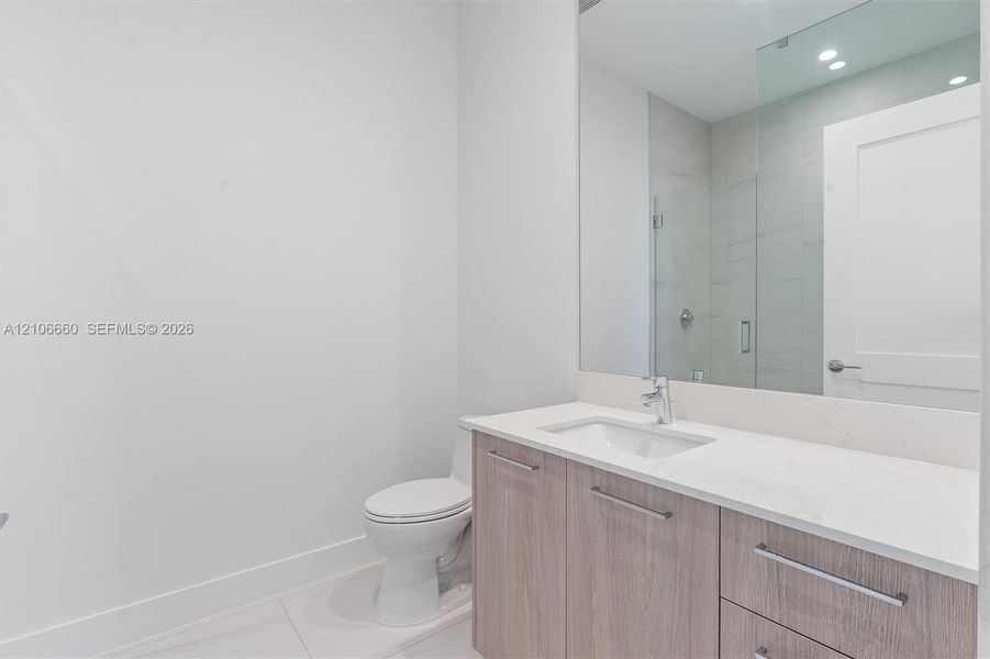 Bathroom featuring a vanity with wood-finish cabinetry, light-toned countertop, undermount sink, large wall-mounted mirror, and glass-enclosed shower