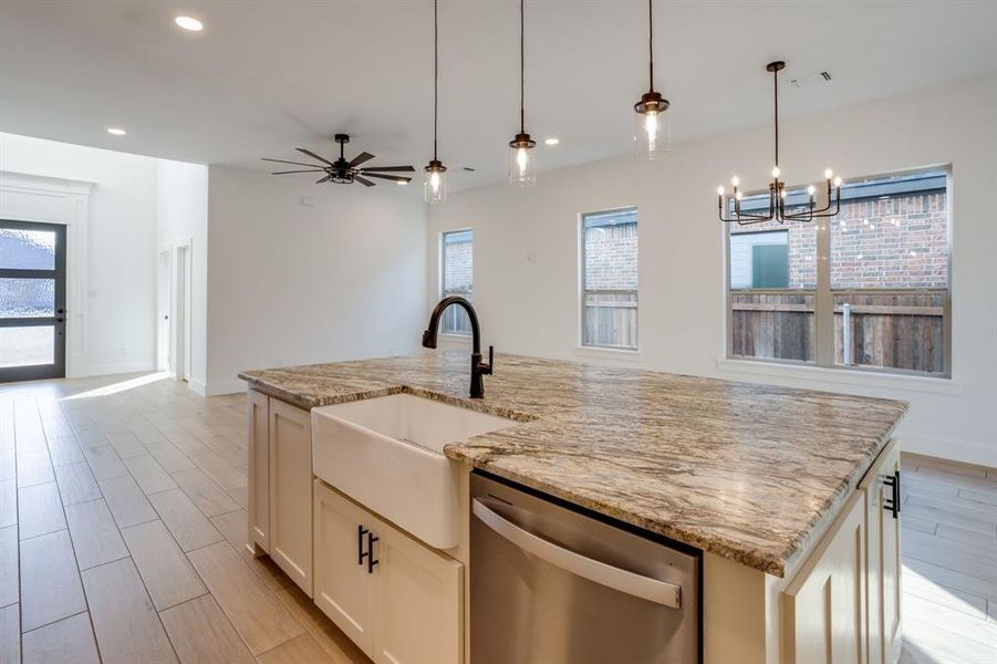 Kitchen featuring dishwasher, wood finish floors, a center island with sink, light stone countertops, and healthy amount of natural light
