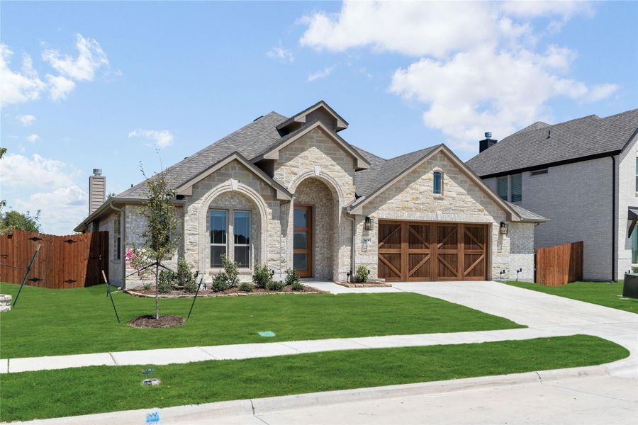 Single-story home with stone exterior, arched entry, wood garage doors, and manicured front lawn