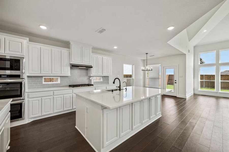 Kitchen with dark hardwood / wood-style floors, a notable chandelier, a kitchen island with sink, sink, and white cabinetry