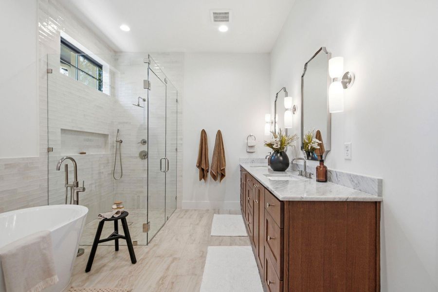 Marble counters and wood cabinetry elevate this primary bath featuring a glass-enclosed shower.