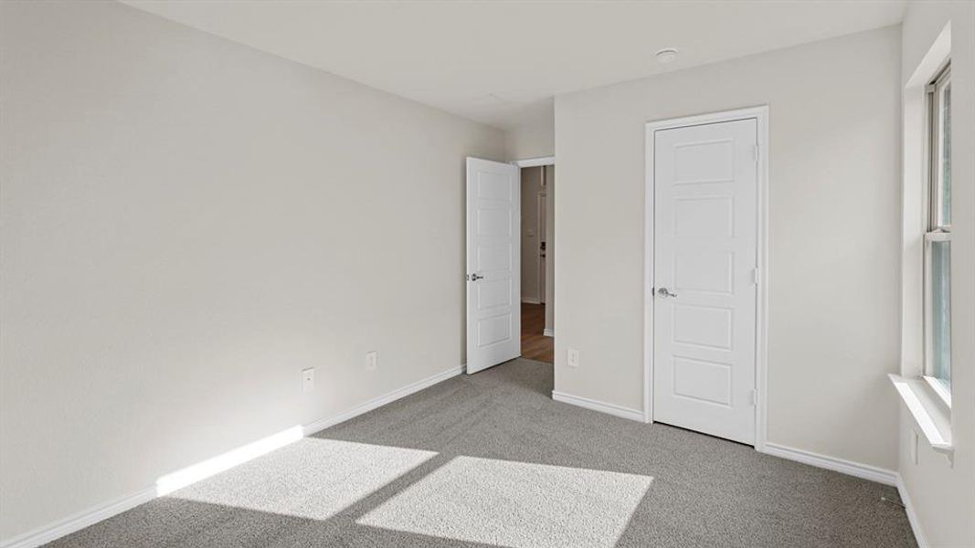 Spacious room featuring light gray carpeting, neutral-toned walls, a multi-paneled door, and a window with a white sill