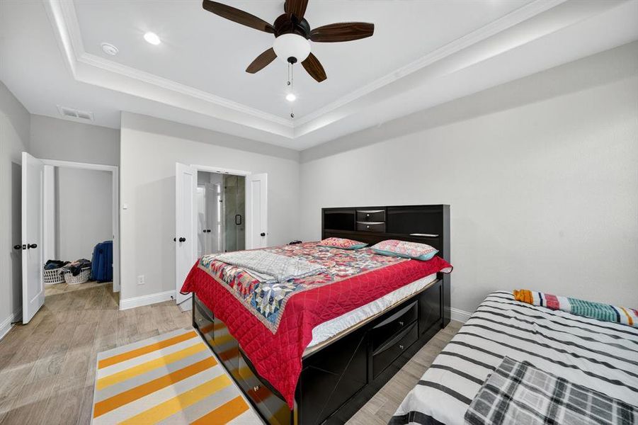 Bedroom with light wood-type flooring, a raised ceiling, crown molding, ceiling fan, and recessed lighting