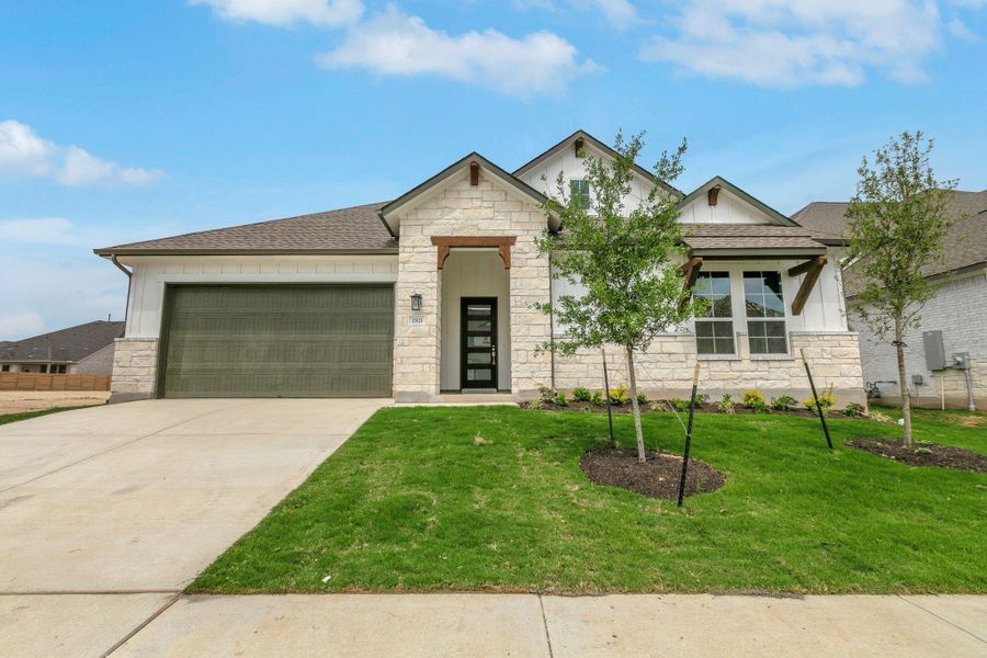 View of front of property with a front yard, an attached garage, stone siding, driveway, and roof with shingles View of front of property with a front yard, an attached garage, stone siding, driveway, and roof with shingles