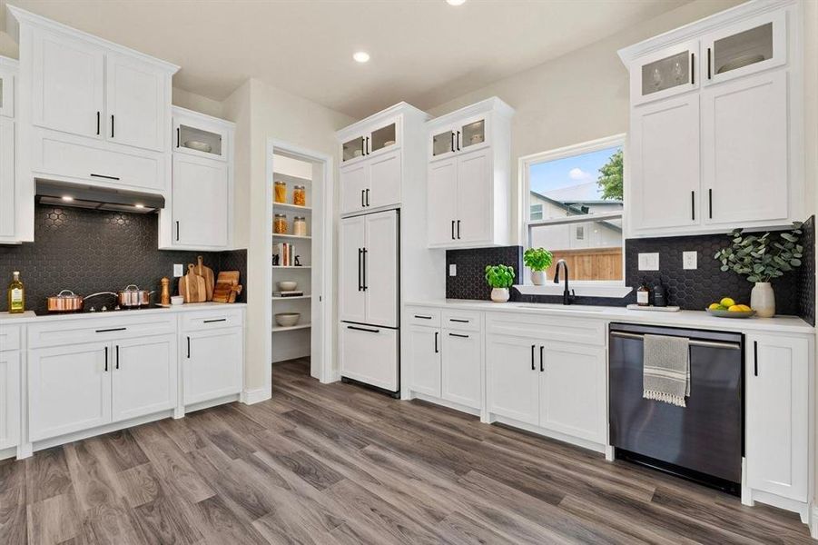 Contemporary kitchen featuring white cabinetry, dark hexagonal tile backsplash, wood-finish flooring, built-in appliances, and a dedicated pantry