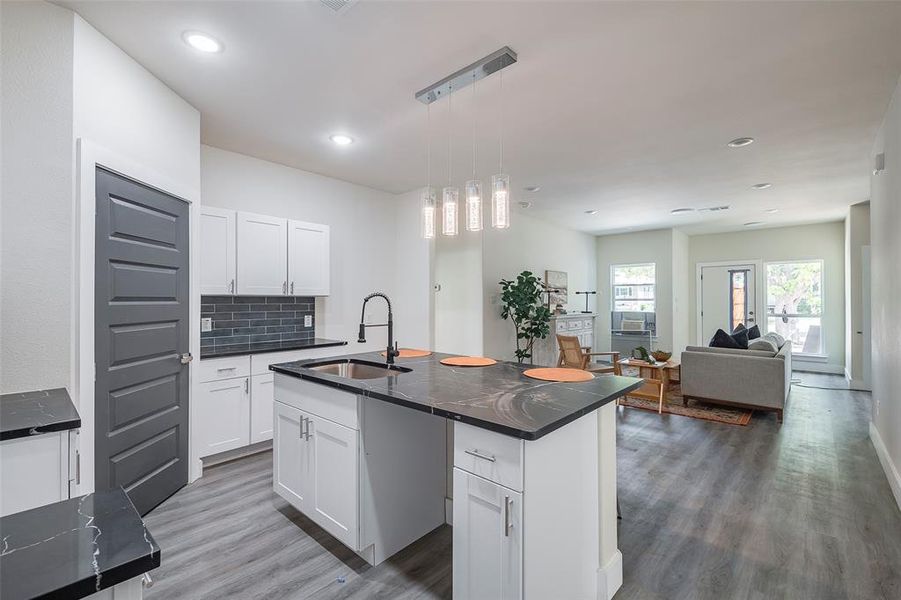 Kitchen featuring pendant lighting, an island with sink, wood-type flooring, white cabinets, and sink