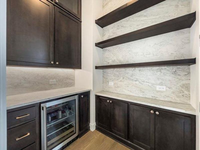 Bar area with backsplash, beverage cooler, light stone counters, light wood finished floors, and open shelves Bar area with backsplash, beverage cooler, light stone counters, light wood finished floors, and open shelves