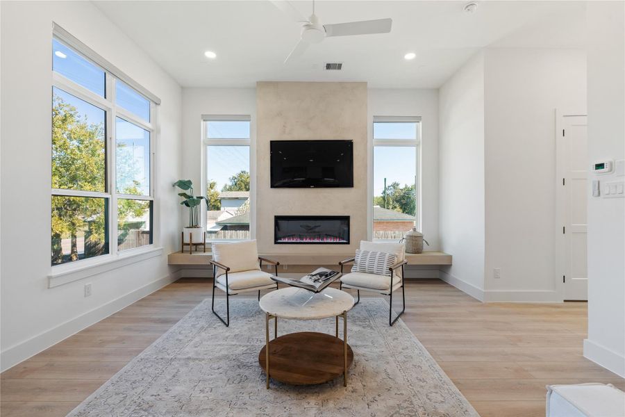 Strategically placed windows frame the living area with natural light, while a centered fireplace wall establishes a strong visual axis that brings cohesion and focus to the room.