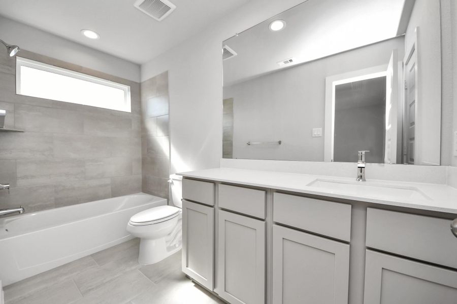 Secondary bath features tile flooring, bath/shower combo with tile surround, light stained wood cabinets, beautiful light countertop.