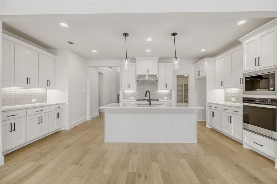 Kitchen featuring stainless steel appliances, hanging light fixtures, an island with sink, light wood finished floors, and white cabinets