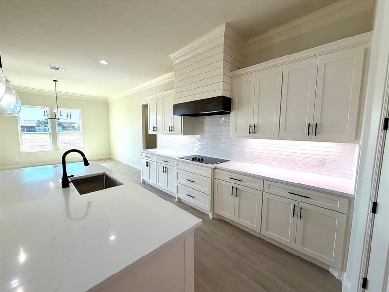 Kitchen with white cabinets, ornamental molding, light stone counters, wood finished floors, and a chandelier Kitchen with white cabinets, ornamental molding, light stone counters, wood finished floors, and a chandelier