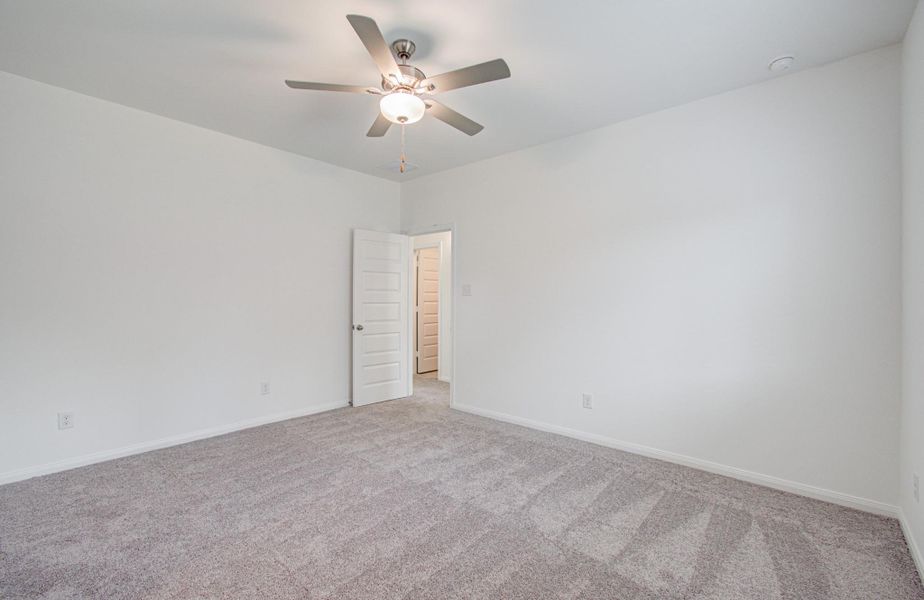 Spacious bedroom with plush carpeting, a modern ceiling fan, and clean white walls, offering a bright and inviting atmosphere.
