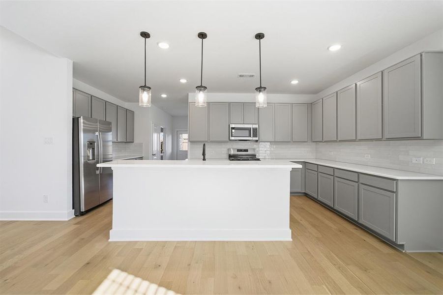 Kitchen featuring a central island, grey cabinetry, stainless steel appliances, light countertops, and wood-finish flooring Kitchen featuring a central island, grey cabinetry, stainless steel appliances, light countertops, and wood-finish flooring