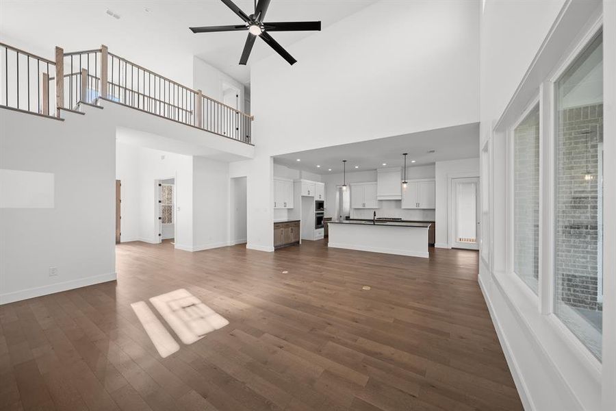 Unfurnished living room featuring dark wood finished floors, a ceiling fan, and a towering ceiling