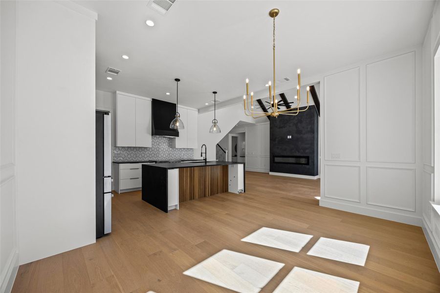 Two tone kitchen featuring modern cabinets, a center island with sink, a chandelier, light wood finished floors, and freestanding refrigerator Two tone kitchen featuring modern cabinets, a center island with sink, a chandelier, light wood finished floors, and freestanding refrigerator