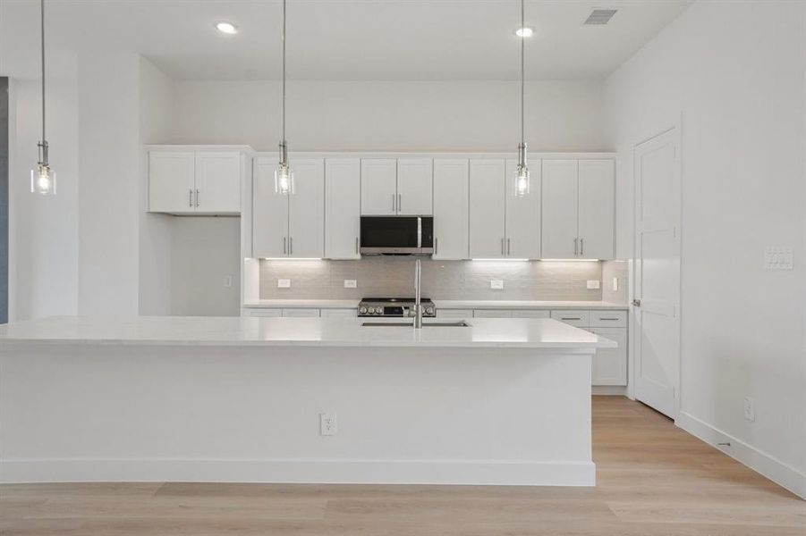 Kitchen featuring white cabinetry, a spacious island, light wood-style flooring, backsplash, and hanging light fixtures