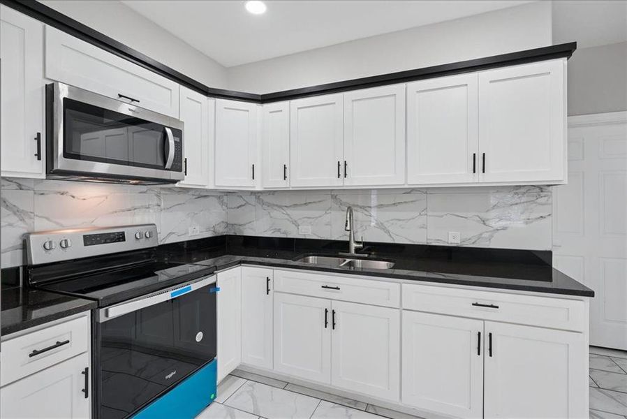 Kitchen with stainless steel appliances, decorative backsplash, light marble finish floors, white cabinetry, and recessed lighting