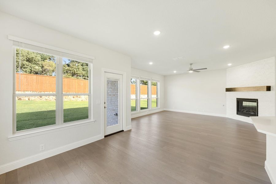 Open living room with hardwood floors, fireplace, ceiling fan, and large windows overlooking backyard