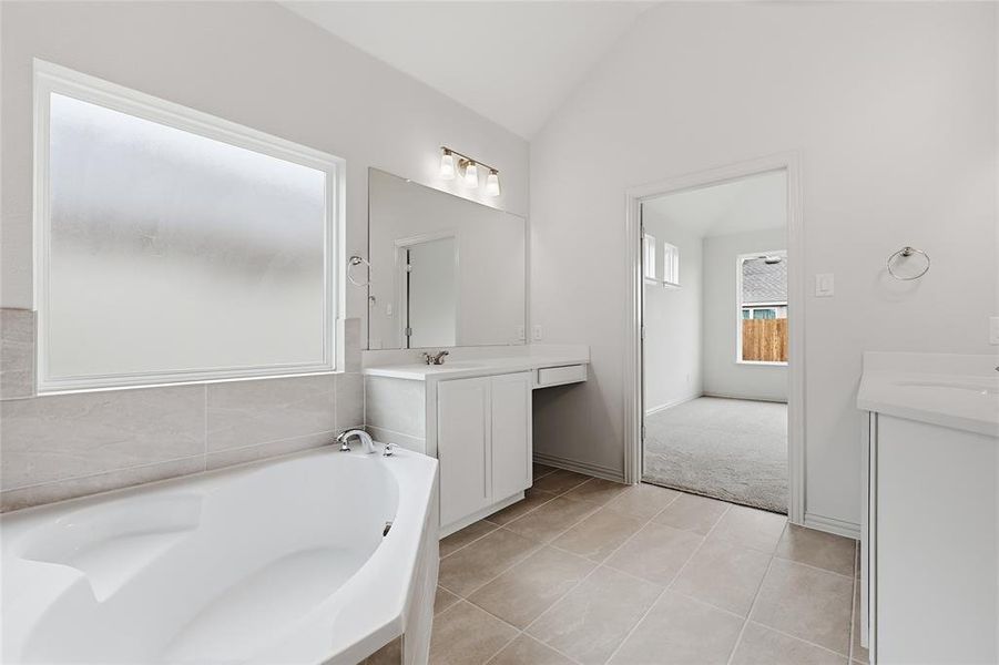 Contemporary bathroom featuring a built-in soaking tub with tile surround, a large frosted window, dual white vanities with integrated sinks, and neutral tile flooring