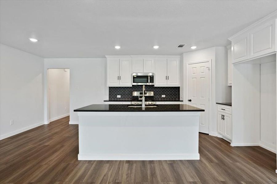 Kitchen with decorative backsplash, dark hardwood / wood-style flooring, white cabinets, and an island with sink