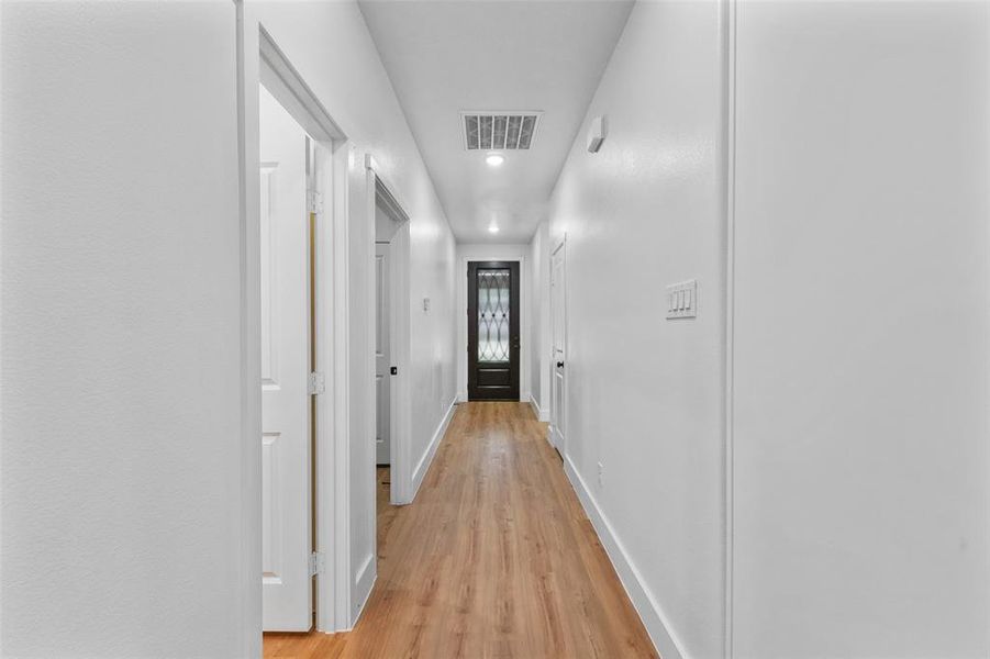 Hallway featuring wood-finish flooring, recessed lighting, white walls, and a black paneled door with decorative glass Hallway featuring wood-finish flooring, recessed lighting, white walls, and a black paneled door with decorative glass