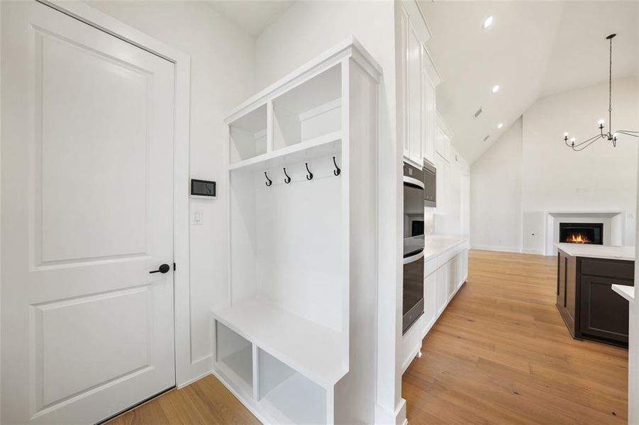 Mudroom with light wood-style floors, a chandelier, recessed lighting, high vaulted ceiling, and a warm lit fireplace