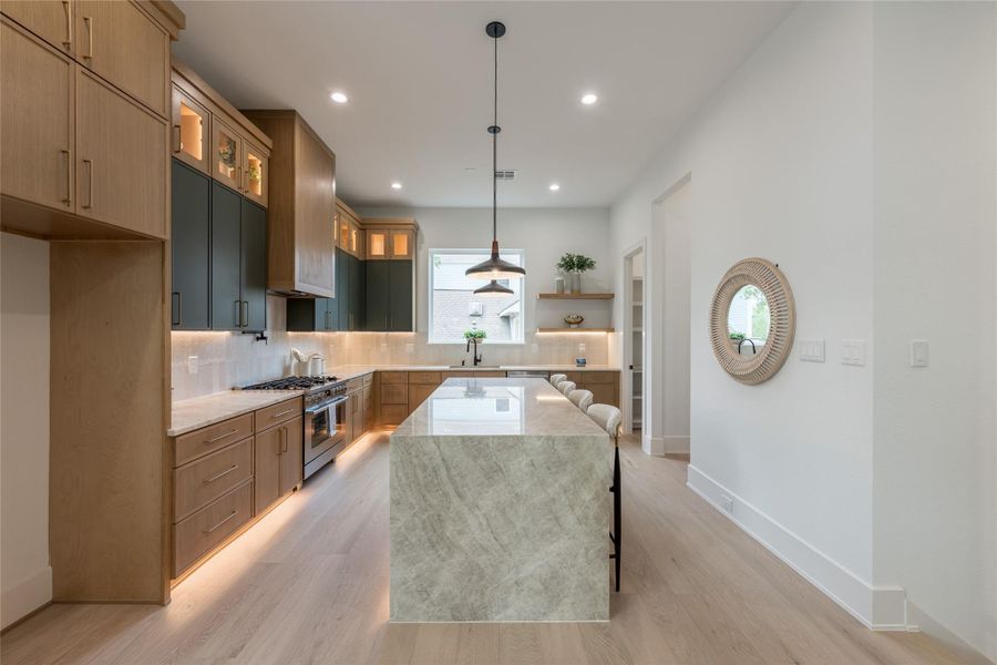 The island does the speaking. A single slab of heavily-figured quartzite, cut and returned at both ends to form a continuous waterfall, carries the room on its own. Everything else calibrated in lower registers to let it sing.