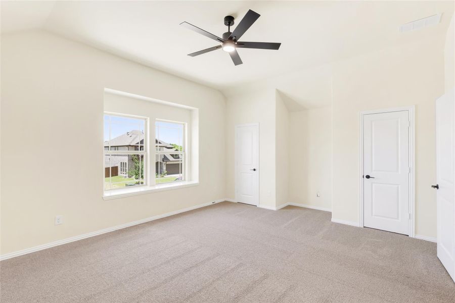Empty bedroom with vaulted ceiling, ceiling fan, carpet flooring, and two white doors Empty bedroom with vaulted ceiling, ceiling fan, carpet flooring, and two white doors