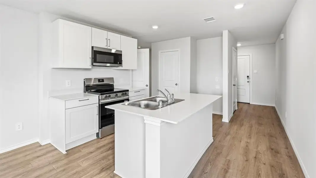 Kitchen featuring stainless steel appliances, white cabinets, light countertops, a kitchen island with sink, and light wood-style flooring