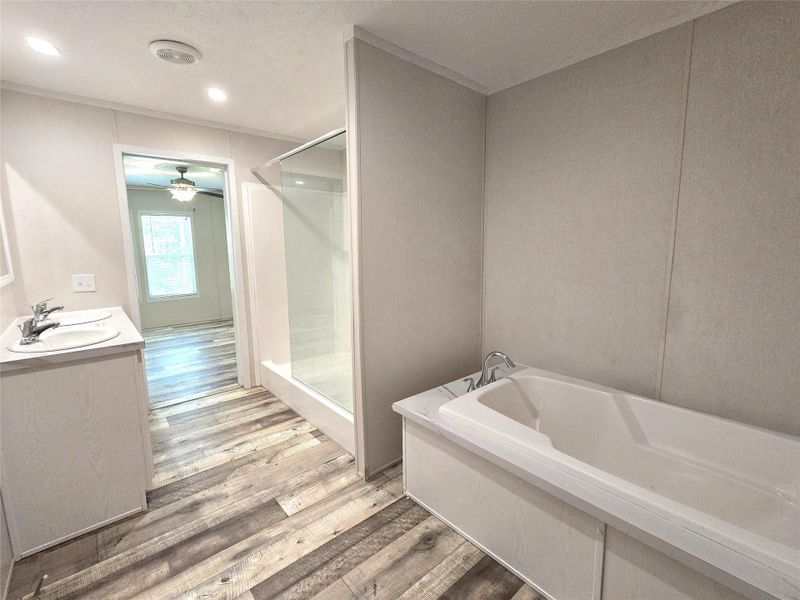 Discover a serene master bath featuring a luxurious soaking tub, sleek shower, and elegant dual sinks, all complemented by warm, inviting wood-look flooring. Discover a serene master bath featuring a luxurious soaking tub, sleek shower, and elegant dual sinks, all complemented by warm, inviting wood-look flooring.