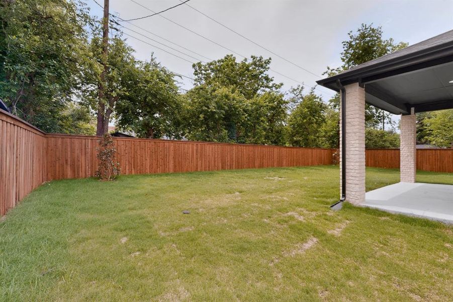 Spacious backyard featuring a manicured lawn, full wood privacy fencing, and a covered concrete patio with brick-clad columns