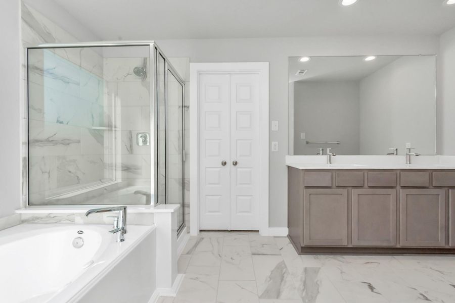 Escape to a spa-like oasis in this primary bathroom. Enjoy a walk-in shower with tile surround, a separate garden tub with custom detailing, and an elegant vanity featuring light countertops, modern hardware, and recessed lighting. Experience luxury and relaxation in every detail. Sample photo of completed plan. As-built color and selections may vary. Escape to a spa-like oasis in this primary bathroom. Enjoy a walk-in shower with tile surround, a separate garden tub with custom detailing, and an elegant vanity featuring light countertops, modern hardware, and recessed lighting. Experience luxury and relaxation in every detail. Sample photo of completed plan. As-built color and selections may vary.