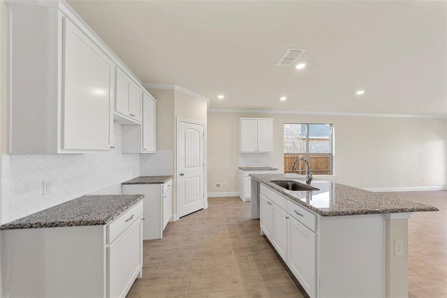 Kitchen featuring stone counters, a center island with sink, white cabinets, sink, and tasteful backsplash