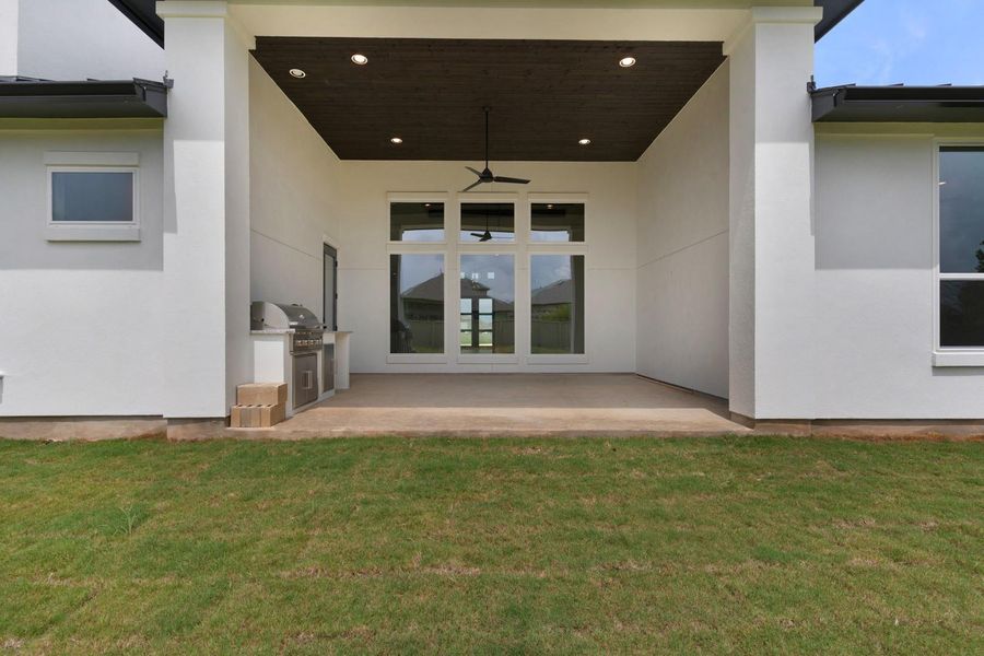 A spacious covered patio with an outdoor kitchen extends into a verdant lawn. A spacious covered patio with an outdoor kitchen extends into a verdant lawn.
