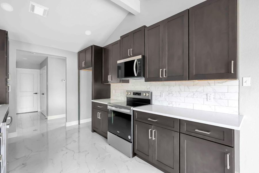 This kitchen features modern dark wood cabinets, sleek countertops, and stainless steel appliances. The space is brightened by a white tile backsplash and glossy marble-style flooring, creating a clean and contemporary look.