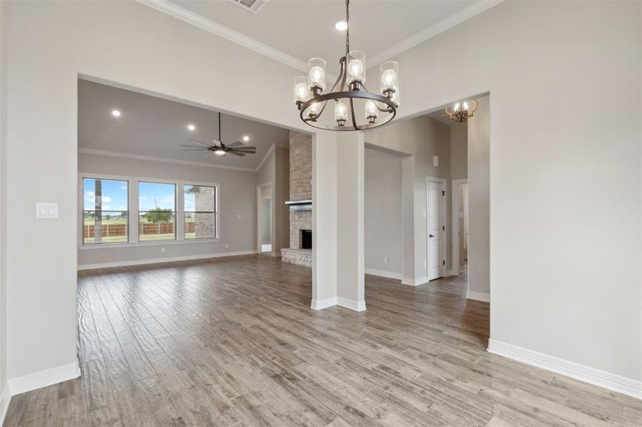 Unfurnished dining area with lofted ceiling, a fireplace, ceiling fan with notable chandelier, crown molding, and light hardwood / wood-style floors