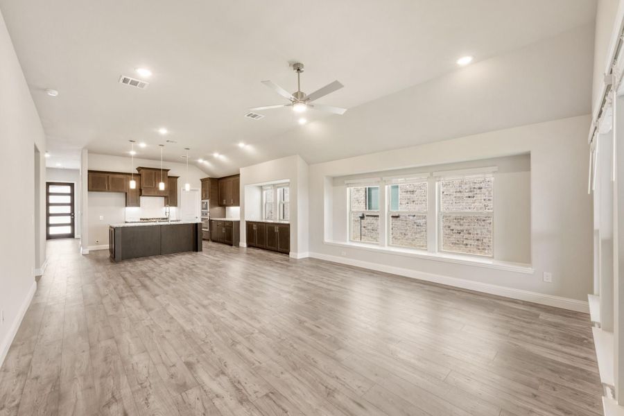 Open-concept living area with light wood floors, ceiling fan, and kitchen with dark cabinets and island in background.