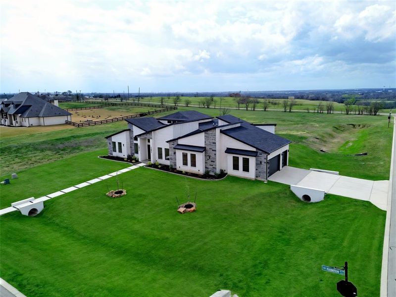 Aerial view showcasing the expansive 1-acre corner homesite and modern transitional architecture, with over 300 acres of scenic farmland creating a peaceful and private backdrop. Grass is digitally enhanced.