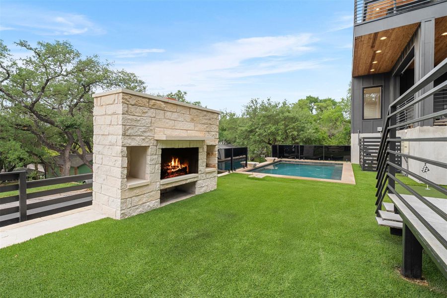 The property features a well-maintained lawn, a stone outdoor fireplace, and a swimming pool
