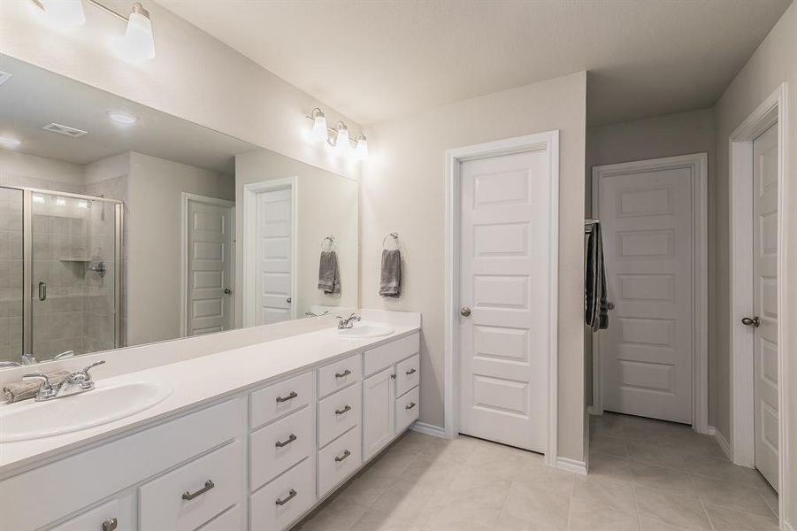 Full bath featuring a shower stall, double vanity, a closet, and light tile patterned floors